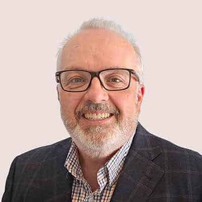 Professional portrait of a smiling senior man with glasses and a checkered shirt.