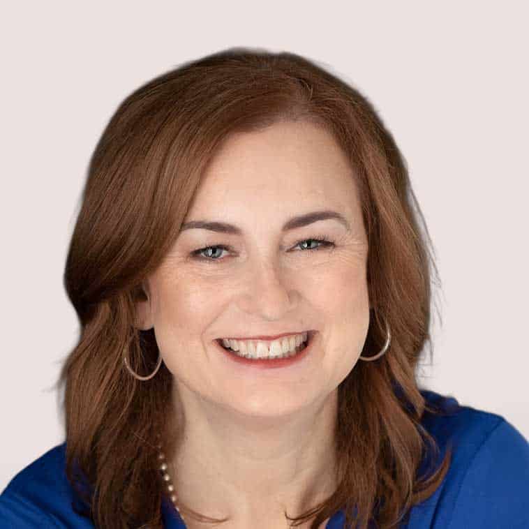 Smiling woman with red hair wearing a blue top and hoop earrings.